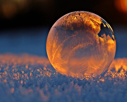 Close-up shot of a frozen bubble with warm reflections resting on a snowy surface at twilight.